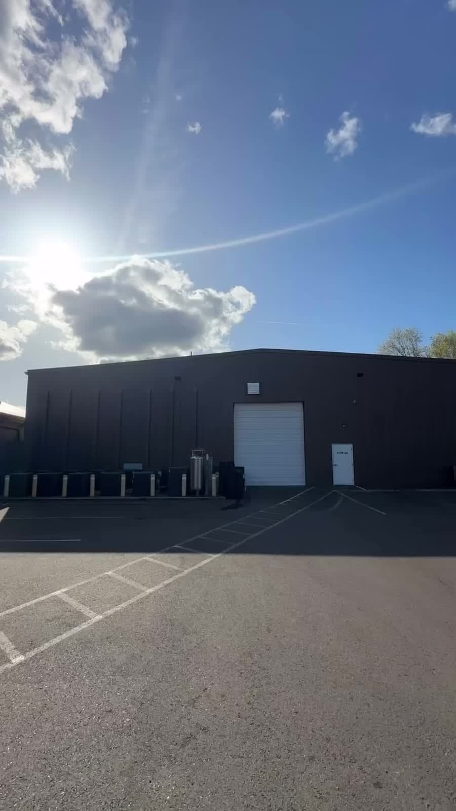 Exterior view of a dark industrial building with a roll-up door and parking lot in afternoon light