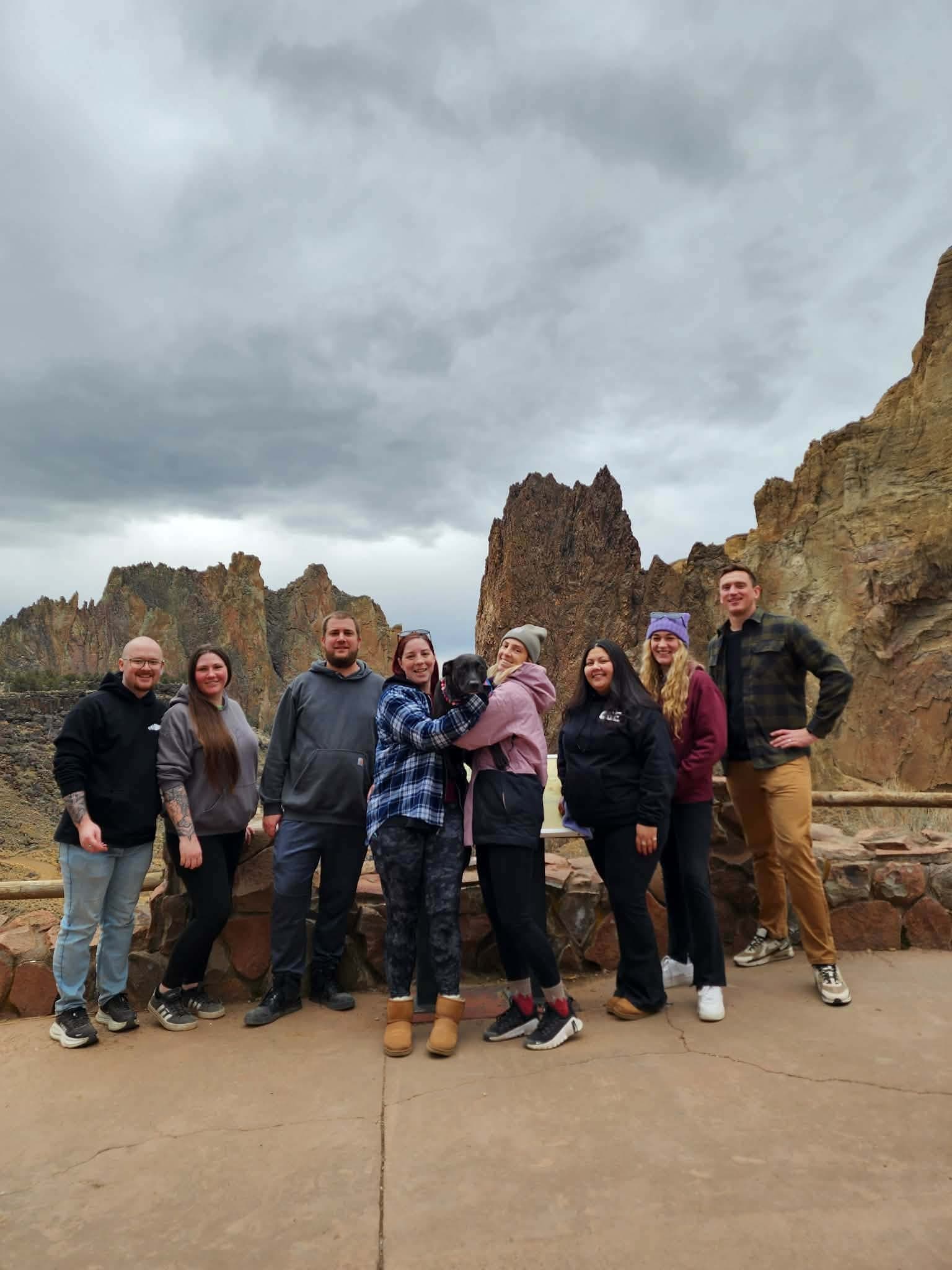 Oregon Greens team members posing outdoors in front of rock formations with a dog